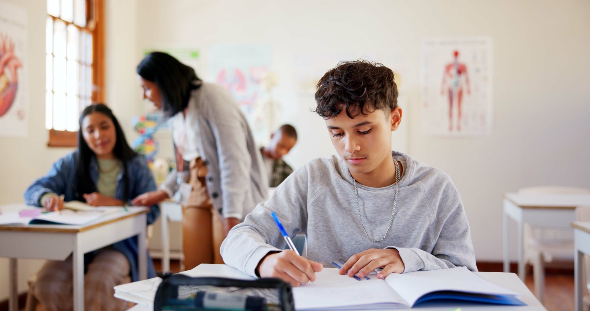 Boy, student and writing with book in classroom for education, learning or exam at school. Young, m